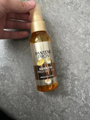 Pantene Pro-V Keratin Protect Oil - Pantene Pro-V Keratin Protect Oil är en hårolja i en genomskinlig plastflaska med pump. Oljan är gyllene och flaskan har guldfärgade detaljer. Perfekt för att vårda och skydda håret med keratin och ge extra glans.