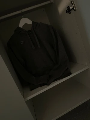 Mörkgrå hoodie från Kappa - Snygg mörkgrå hoodie från Kappa med klassisk logga på bröstet. Hoodien har dragsko i huvan och är tillverkad i mjukt material, perfekt för en avslappnad stil. Passar dig som gillar streetwear och enkel design.