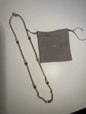 Guldfärgat (roseguld) halsband Michael Kors - Snyggt guldfärgat halsband från Michael Kors med kedjedesign och dekorativa fyrkantiga detaljer längs hela halsbandet. Kommer med en grå tygpåse med logga. Perfekt accessoar för att lyfta din outfit. 78 cm 