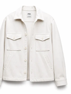 Vit overshirt från ZARA - Stilren vit overshirt från ZARA med klassisk krage, raka ärmar och fyra fickor framtill, varav två med lock och knapp. Overshirten har knäppning framtill och är tillverkad i ett mjukt, tjockare tyg som ger en avslappnad look.