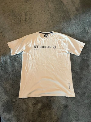 Beige t-shirt - Beige t-shirt med svart texttryck på bröstet och liten detalj vid nederkanten. Klassisk rund hals och kortärmad. Tyvärr lite defekter(se bilder). Skriv om du har funderingar !