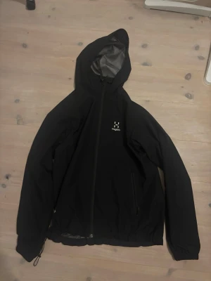 Haglöfs Jacka - !!!!!!!!!Size M Women!!!!!!!!!!Snygg svart vindjacka från Haglöfs med hel dragkedja, justerbar huva och dragsko i nederkant. Jackan har två sidofickor med dragkedja och meshfoder på insidan av huvan. Perfekt för blåsiga dagar och outdoor-aktiviteter.