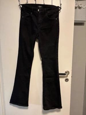 Svarta bootcut jeans från ONLY - Säljer ett par svarta bootcut jeans från ONLY med klassisk femficksmodell och hög midja. Jeansen har utsvängda ben och är tillverkade i ett mjukt denimtyg som sitter snyggt. Perfekta för dig som gillar en tidlös och trendig look.