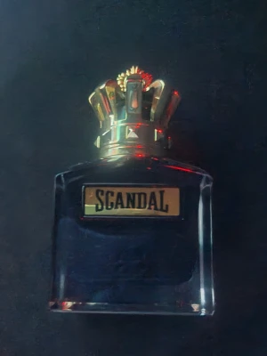 Scandal Le Parfum Pour Homme 100ml - Scandal Le Parfum Pour Homme från Jean Paul Gaultier är en intensiv herrparfym i en elegant mörk glasflaska med en guldig krona som lock. Flaskan har en lyxig känsla och etiketten är i guld med svart text. Perfekt för dig som gillar exklusiva dofter.