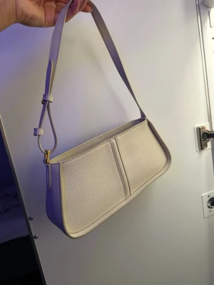 Beige axelväska  - Stilren beige axelväska med justerbart axelband och minimalistisk design. Väskan har en fin form, Perfekt för dig som gillar enkel och clean stil.
