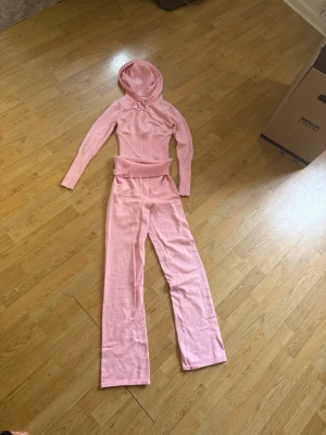 Rosa mjukisdress med huva - Säljer en supermysig rosa loungewear-set i mjukt stickat material. Setet består av en långärmad hoodie med huva och matchande byxor med resår i midjan. Perfekt för chill dagar hemma eller när du vill vara extra bekväm.