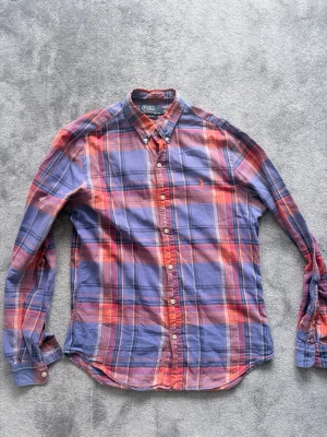 Rutig skjorta i lila och rött - Sjukt snygg skjorta från Ralph Lauren i slim fit M. Inga skavanker förutom ett litet hål i armhålan, kan enkelt sys ihop med några stygn. Riktigt snygg cloorway med lila röd och orange. Jag är 190 cm och den är kort på mig, om du är runt 185 nånting lär den passa sjukt bra