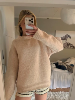 Beige/rosa oversized stickad tröja - Mysig beige/rosa stickad tröja med oversized passform och rund hals. Tröjan har långa ärmar och ribbade muddar vid ärmslut och nederkant. Perfekt för lager på lager och chill dagar. Materialet ser ut att vara mjukt och fluffigt.