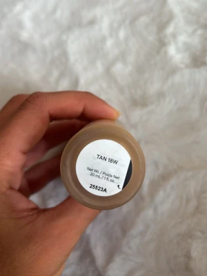 Foundation TAN 18W i glasflaska - Foundation i nyansen TAN 18W, förpackad i en stilren glasflaska med vit kork. Flaskan rymmer 30 ml och har en frostad finish med stora vita bokstäver på utsidan. Perfekt för dig som vill ha en varm, tan-tonad bas. Använd 1 gång.