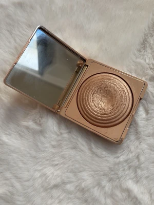CAIA Highlighter Portofino guld - Säljer en CAIA Highlighter i nyansen Portofino. Kommer i en lyxig, fyrkantig guldfärgad dosa med spegel. Själva highlightern har en skimrande guldton och är pressad i ett vågmönster. Perfekt för att ge glow till ansiktet.
