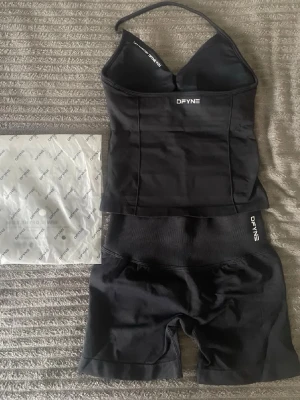DFYNE impact set i svart - Säljer ett svart shaping-set från DFYNE som består av en figurnära topp med smala axelband och matchande höga shaping-shorts. Setet har en stilren design med logga framtill och är gjort i ett stretchigt, mjukt material som formar kroppen. Perfekt för dig som vill ha en smickrande siluett.