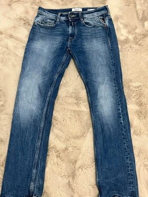 Blå raka jeans med kontrastsömmar - Säljer ett par klassiska blå jeans med raka ben och snygga slitningar framtill. Jeansen har fem fickor och kontrastsömmar på bakfickorna som ger en cool detalj. Tillverkade i denim med en autentisk tvättad look. Perfekta till en avslappnad stil.