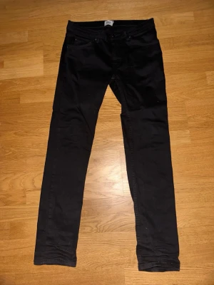 Svarta skinny jeans midja 31 längd 32 - Säljer ett par svarta skinny jeans med klassisk femficksdesign och smal passform. Jeansen har midja 31 och längd 32. Perfekta för dig som gillar en stilren och enkel look. Materialet känns mjukt och stretchigt för extra komfort.