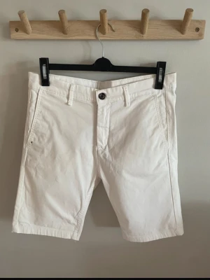 Vita klassiska bomullsshorts - Snygga vita shorts med normal passform och midja. De har fickor på sidorna, bälteshällor och stängs med knapp och dragkedja. Perfekta för varma dagar och enkla att matcha med olika stilar. Är helt oanvända, som nya! Kontakta gärna för frågor!