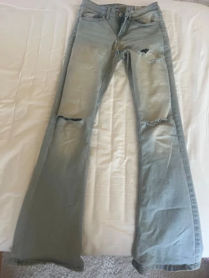 Ljusblåa low flare jeans XS L32 - Säljer ett par ljusblåa low flare jeans med slitningar och hål på knäna. Jeansen har låg midja och utsvängda ben, perfekt för en trendig och avslappnad look. Materialet är klassisk denim i bomull. Snygga att matcha med sneakers eller boots. Men är lite slitna men funkar fortfarande 🩵