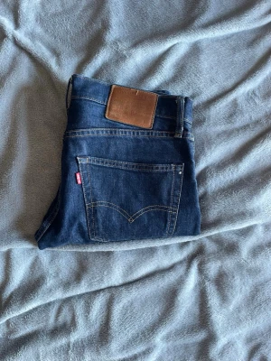 Levis 502 - Snygga mörkblå jeans med raka ben och klassisk femficksdesign. Jeansen har en brun läderpatch bak i midjan och en röd etikett på bakfickan. Tillverkade i denim med tydliga sömmar och normalhög midja.