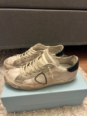 Vita sneakers med svart detalj - Snygga vita sneakers med svart häl och en unik svart detalj på sidan. Skorna har klassisk låg profil, vita snören och slitna detaljer för en cool, avslappnad look. Perfekta för dig som gillar streetstyle och vill ha något som sticker ut.