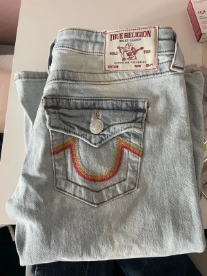 True Religion ljusblå flare jeans - Säljer ett par ljusblå True Religion jeans i modellen Joey Low Rise Flare. har aldrig använt dem, helt nya. Jeansen har ikonisk ficka med färgglad brodyr och knappdetalj. Klassisk femficksmodell i mjuk denim med snygga kontrastsömmar. Perfekta för dig som gillar retrovibbar och unik stil.