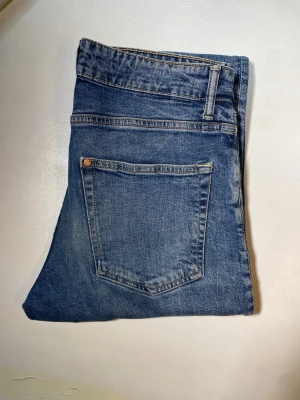 Blå raka jeans med fem fickor - Säljer ett par klassiska blå jeans i rak modell med fem fickor och normal midja. Jeansen har bälteshällor, knappgylf och är gjorda i ett slitstarkt denimtyg. Perfekta för en avslappnad och trendig look.