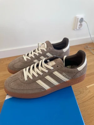 Adidas Spezial sneakers - Snygga Adidas Spezial sneakers i grå mocka med vita detaljer och klassiska tre ränder på sidan. Skorna har en brun gummisula och vita skosnören. Perfekt för dig som gillar retrostil och vill ha något som sticker ut.