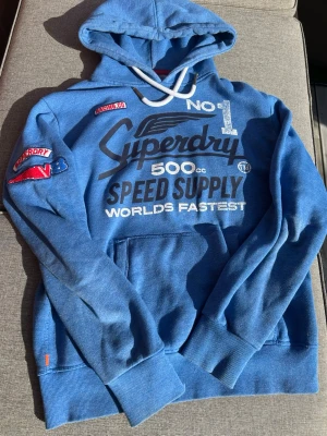 Super dry hoodie - Riktigt fet hoodie från super dry. En väldigt sällsynt hoodie som är svår att få tag på i just detta tryck. Perfekt nu till vintern och hösten då den håller en riktigt varm. På armen så finns det två märken sydda som gör tröjan ännu fetare. Storlek M.Hör gärna av er om ni undrar något eller om ni vill ha storleks måtten