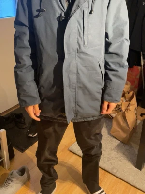 Blå parkasjacka från Canada Goose - Snygg blå parkasjacka från Canada Goose med dragkedja, bröstficka och två sidofickor. Jackan har justerbar huva med snörning och klassisk patch på ärmen. Perfekt för kalla dagar och har en stilren, rak passform.