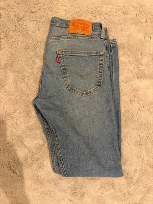 Levi's ljusblå raka jeans - Klassiska ljusblå jeans från Levi's med rak passform och fem fickor. Jeansen har den ikoniska röda Levi's-lappen på bakfickan och patch i läder bak i midjan. Tillverkade i slitstark denim, perfekta för en avslappnad och tidlös stil.