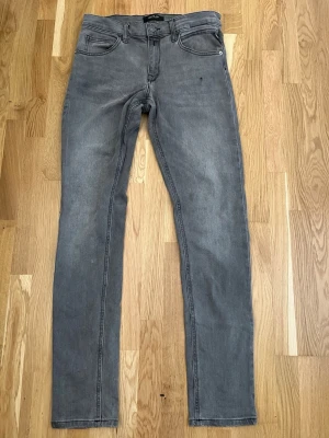 Grå raka jeans med fem fickor - Snygga grå jeans med rak passform och klassisk femficksdesign. Jeansen har bälteshällor, dragkedjegylf och subtila sömdetaljer på bakfickorna. Perfekta för en avslappnad och stilren look.