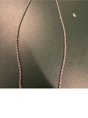 Tunt tvinnat silverfärgat halsband - Säljer ett stilrent halsband i silverfärg med tvinnad kedja. Halsbandet har en enkel och elegant design som passar perfekt till olika stilar. Materialet ser ut att vara metall och kedjan är smal och diskret.