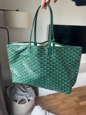 Grön shoppingväska - Snygg grön shoppingväska med klassiskt mönstr i vitt och grönt. Väskan har två långa handtag och är i perfekt storlek för att få plats med allt du behöver under dagen. Mått 50x27. Finns gulgrön fläck i botten som syns på bild 4 och 5. Ej aut3ntisk. 