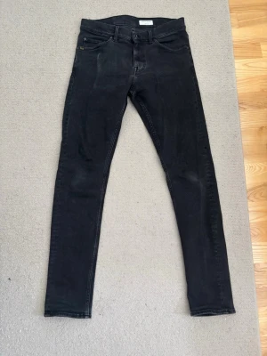 Svarta slim-fit jeans från tiger of sweden - Säljer ett par svarta jeans i slim-fit modell. Jeansen har smal passform hela vägen ner och är tillverkade i stretchigt material. Perfekta för dig som gillar en slimmad look. Personen på bild är 193cm lång