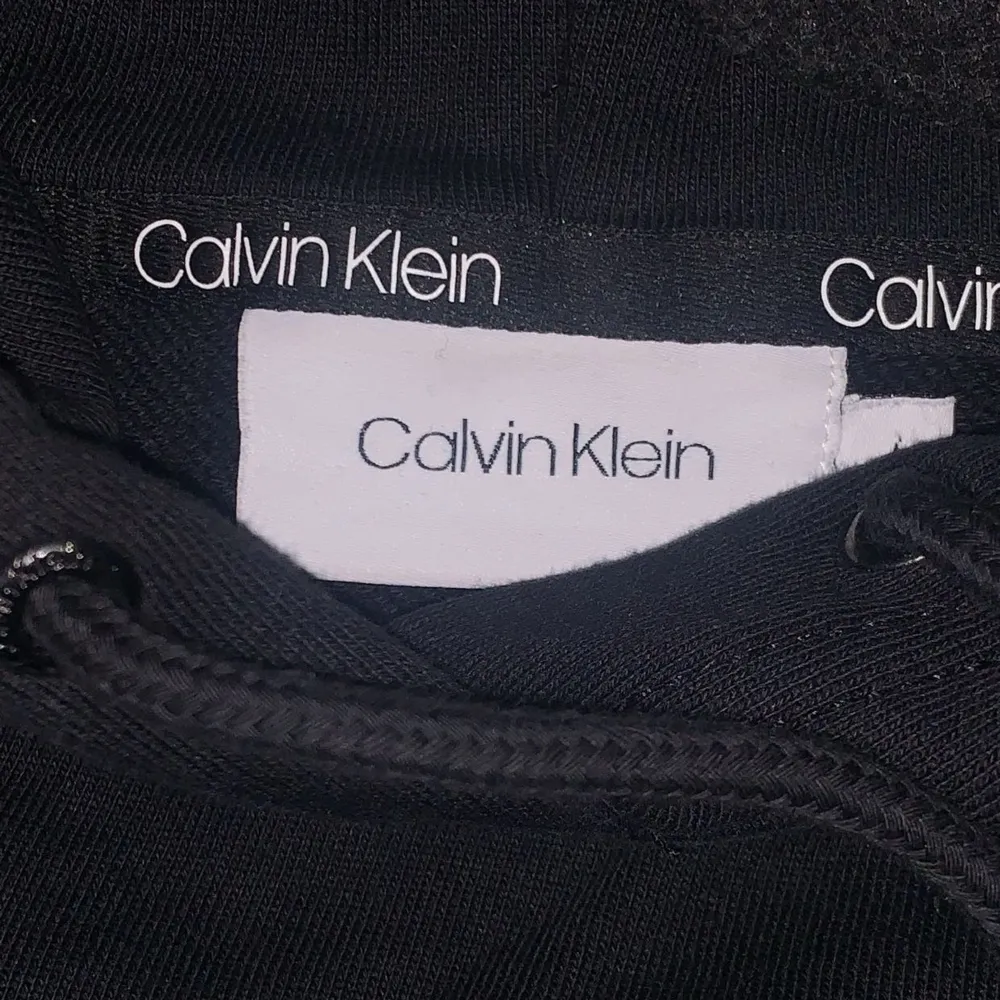 Säljer en stilren svart hoodie från Calvin Klein. Den har en klassisk passform med justerbar huva och det ikoniska Calvin Klein-logotypen tryckt på framsidan. Perfekt för en avslappnad look eller att mysa i hemma. Passar till alla säsonger!. Neuletakit & Villapaidat.