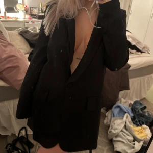 Svart kavaj - Säljer en stilren svart kavaj klänning i bra skick. Perfekt för både fest och vardag. Kavajen har en klassisk design med knappar framtill och långa ärmar. Passar till många olika outfits och tillfällen. Har även axelvaddar