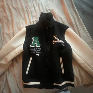  jacka från Axel Arigato - Säljer en snygg jacka från Axel Arigato i storlek L. Jackan har vita ärmar och broderade detaljer fram och bak. Perfekt för höst och vår med sin stilrena design och bekväma passform!