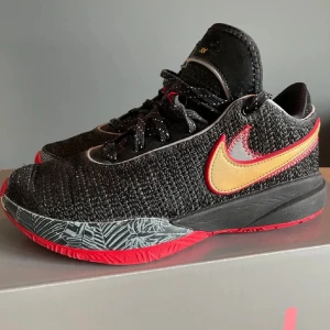 Svarta och röda Nike sneakers - Snygga Nike sneakers i svart med röda och guldiga detaljer. Skorna har en cool mönstrad sula och en ikonisk Nike-logga på sidan. Perfekta för både vardag och träning. De är i mycket bra skick och redo för nya äventyr!