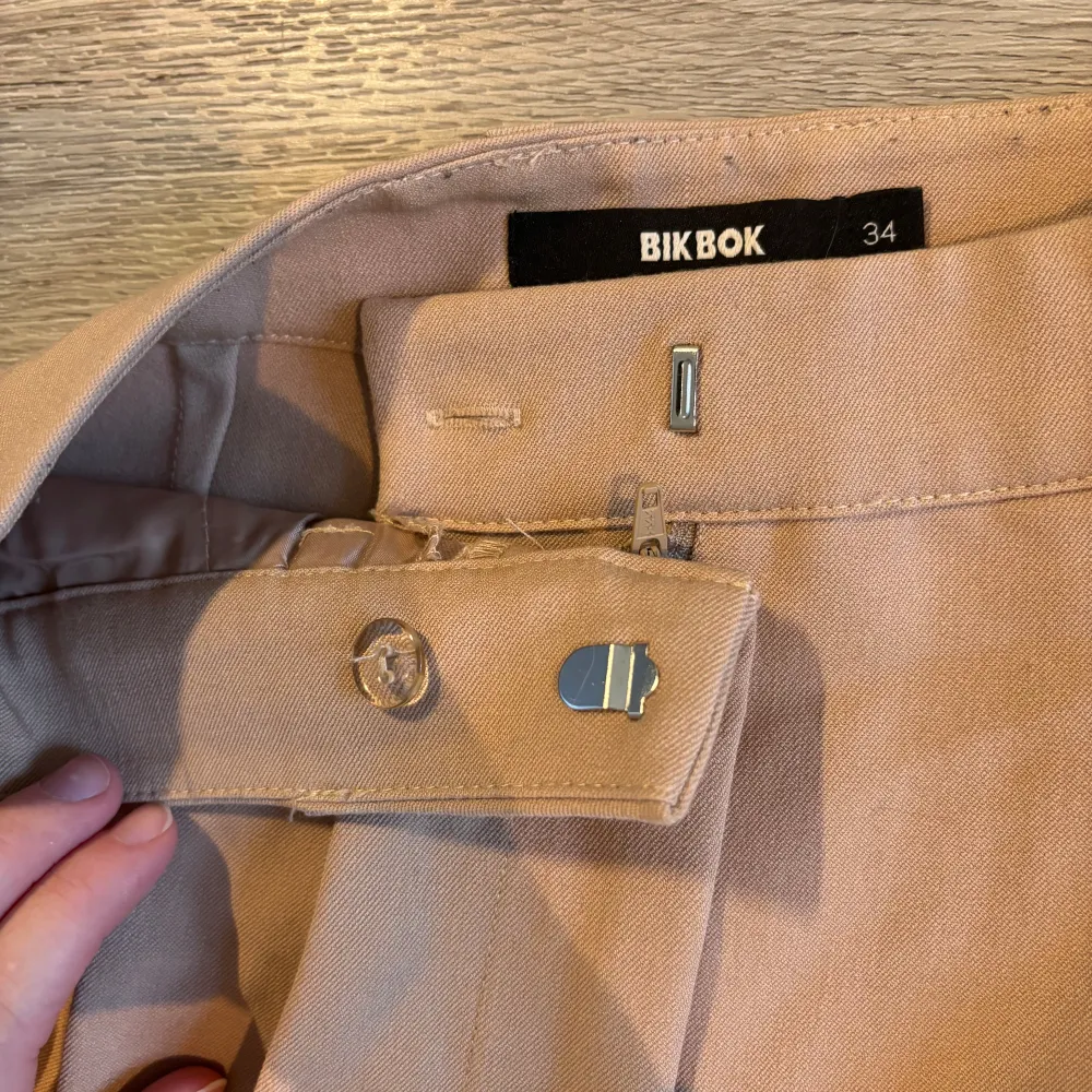 Säljer ett par snygga beige kostymbyxor från BikBok i storlek 34. De är högmidjade med en klassisk rak passform och har knäppning fram. Perfekta för både vardag och fest! 🕺. Jeans & Byxor.