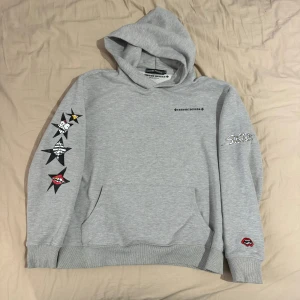Grå hoodie från Chrome Hearts (OBS XL passar som M) - Säljer en grå hoodie från Chrome Hearts med coola tryck på ärmarna och ryggen. Den har en känguruficka och är perfekt för en avslappnad stil. Tillverkad i USA och i bomullsmaterial, vilket gör den både bekväm och hållbar. Perfekt för höst och vår!