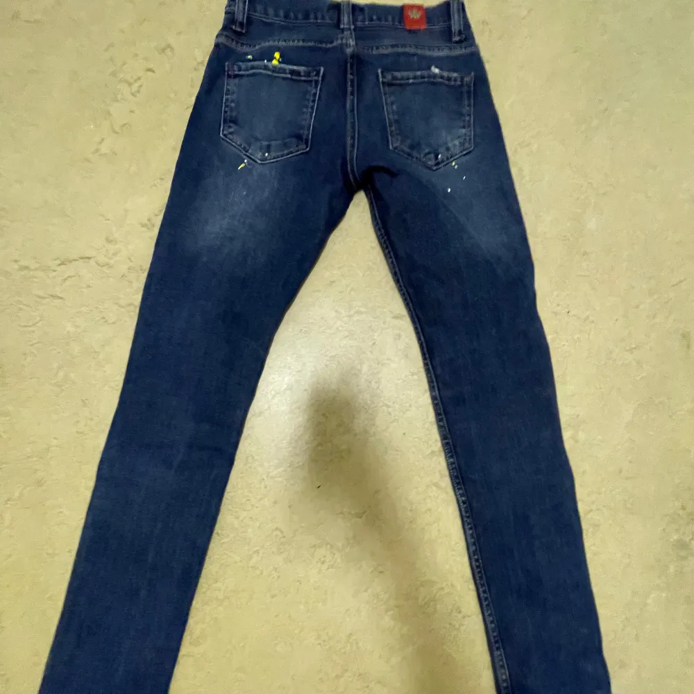 Säljer ett par snygga blå jeans från DSquared2 med coola slitningar och detaljer. De har en slim passform och är perfekta för både vardag och fest. Jeansen har en klassisk femficksdesign och en knappgylf. Märkeslogga syns på baksidan. Passar perfekt för dig som vill ha en stilren men ändå edgy look.. Jeans & Byxor.