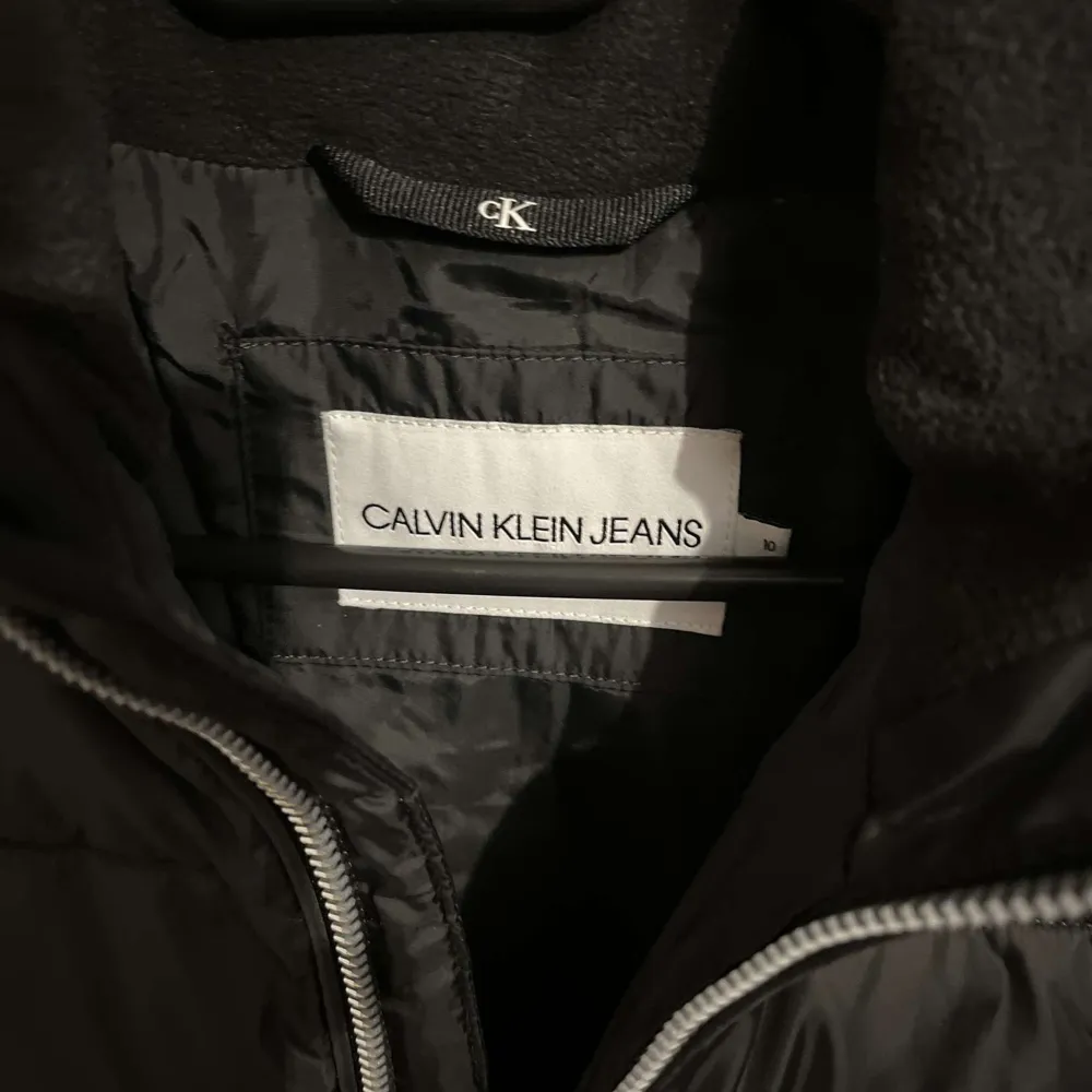 Säljer en snygg svart pufferjacka från Calvin Klein i mycket bra skick. Jackan har en dragkedja framtill och en mysig huva. Perfekt för kalla dagar och håller dig varm och stilren. Stor logga på bröstet ger en cool touch. Passar perfekt till både vardag och fest!. Jackor.