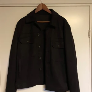 Jacka - Säljer en stilren mörk mörk mörk brun jacka i mycket bra skick. Den har en klassisk design med knappar framtill och två bröstfickor med lock. Perfekt för höst vår och vinter, och passar både till vardags och lite finare tillfällen. Jackan har långa ärmar och en normal passform.