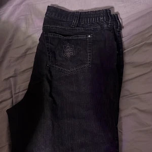 Svarta jeans med broderad bakficka - Säljer ett par snygga svarta jeans i bra skick. De har en broderad detalj på bakfickan som ger en unik touch. Jeansen har en klassisk femficksdesign och är perfekta för både vardag och fest. Passformen är normal och de är gjorda i ett bekvämt denimtyg.