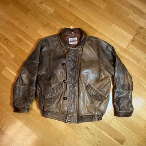 Vintage Brun skinnjacka  - Säljer en vintage brun skinnjacka från Strawberry, perfekt för året om. Jackan har en cool retro look med knappar och quiltad insida för extra värme. Den har en wide passform och är i bra skick, bara att innerfodret i ytterfickorna har hål i borten. Så saker tamlar inte ur fickorna. Sen saknas en knapp, vilket syns på bild 1 men inget jag saknat då jag alltid bärt den öppen eller bara använt dragkedjan. Perfekt för dig som vill ha en unik stil!