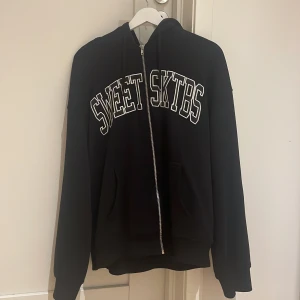 Svart hoodie från Sweet SKTBS - Säljer en svart hoodie från Sweet SKTBS i bra skick. Den har en dragkedja framtill och stora fickor. Perfekt för höst och vinter, med en skön passform och långa ärmar. Texten 'SWEET SKTBS' är tryckt i vitt på bröstet. Grym för både chill och skate! 🖤storleken är xs men sitter som storlek M