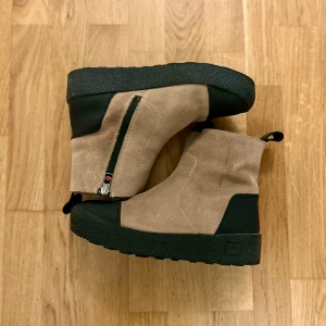 Beige och svarta boots från Canada Snow - Säljer ett par snygga och varma boots från Canada Snow i beige mocka med svarta detaljer. De har en praktisk dragkedja på sidan och är fodrade med mjuk ull för extra värme. Perfekta för kalla vinterdagar! Skorna är köpta på Scorett för 2500kr. 