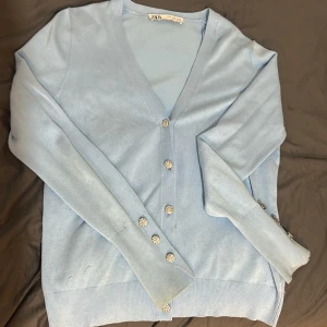 Ljusblå kofta från Zara - Säljer en superfin ljusblå kofta från Zara. Den har en v-ringad design med glittriga knappar framtill och på ärmarna. Perfekt för både vardag och fest! 💙Lite använd men annars i jättefint skicka. På baksidan av koftan är det lite små vita fläckar men det är inget man tänker på och syns inte alls så mycket speciellt om man har håret nere. Bortsätt från det är den som ny. Säljer pågrund av ej användning och andra likadana koftor. Den är i storlek M men passar även S.