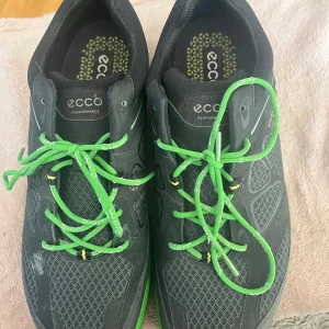 Svarta och gröna sneakers från Ecco - Säljer ett par snygga och sportiga sneakers från Ecco i svart och grönt. Skorna har gröna snören och en robust sula som ger bra grepp. Perfekta för träning eller vardagsbruk. De är helt nya och redo för att bli använda! Prut bart.