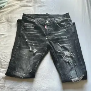 Säljer ett par svarta jeans från Dsquared2 i bra skick. De har en cool distressed look med slitningar och hål, perfekt för en avslappnad stil. Jeansen har en knappgylf och en snygg passform. Märkeslappen 'ICON' på baksidan ger extra attityd. Perfekta för både vardag och fest!