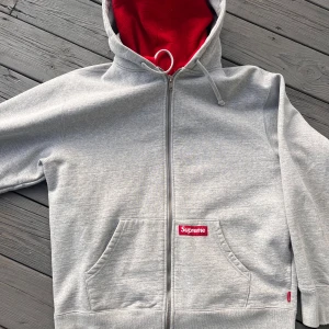 Grå Surpeme double hooded hoodie - Grå Supreme hoodie med en insydd röd mask som funkar som luva också, från F/W 22 och är ganska använd men ändå i bra skick förutom vid hand lederna där det är lite slitage. Nypris-1900