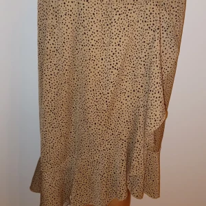 Beige prickig kjol - Säljer en superfin beige kjol med små svarta prickar. Kjolen har en volangdetalj längst ner som ger den en söt och lekfull look. Perfekt för både vardag och fest! 🖤