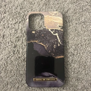 Mobilskal från Ideal of Sweden - Snyggt mobilskal från Ideal of Sweden med ett marmorerat mönster i svart, beige och guld. Skalet har en glansig finish och är designat för att passa perfekt runt din telefon. Perfekt för att ge din mobil en stilren look! Liten skada men annars fel fri🤗